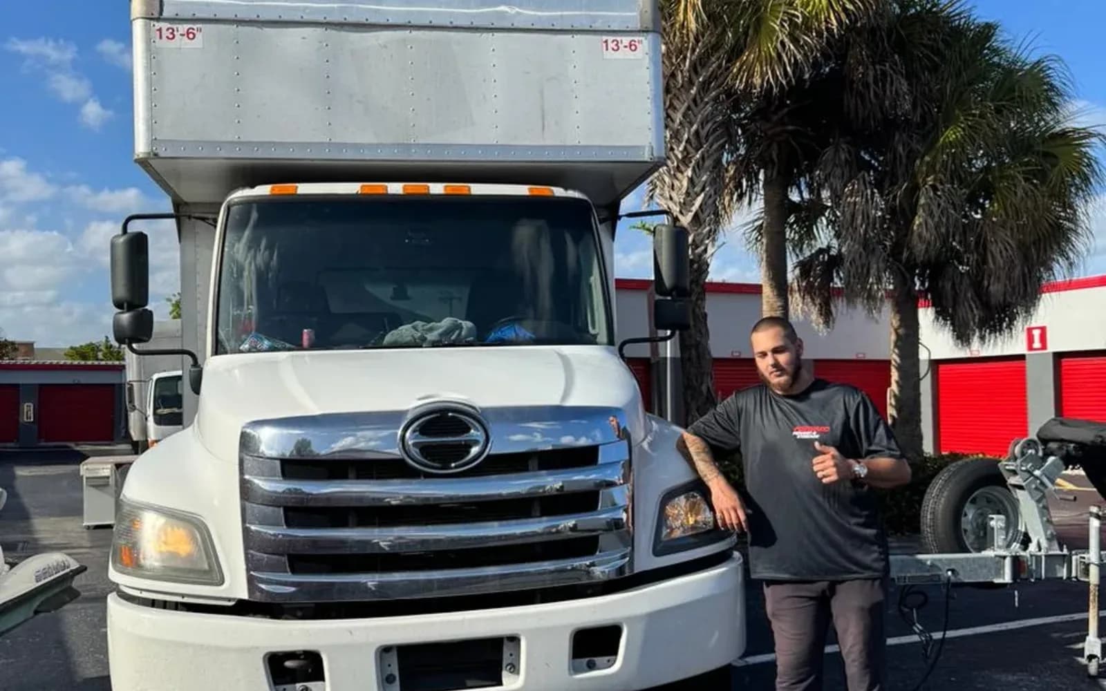 White moving truck with palm trees and a mover standing beside it outdoors