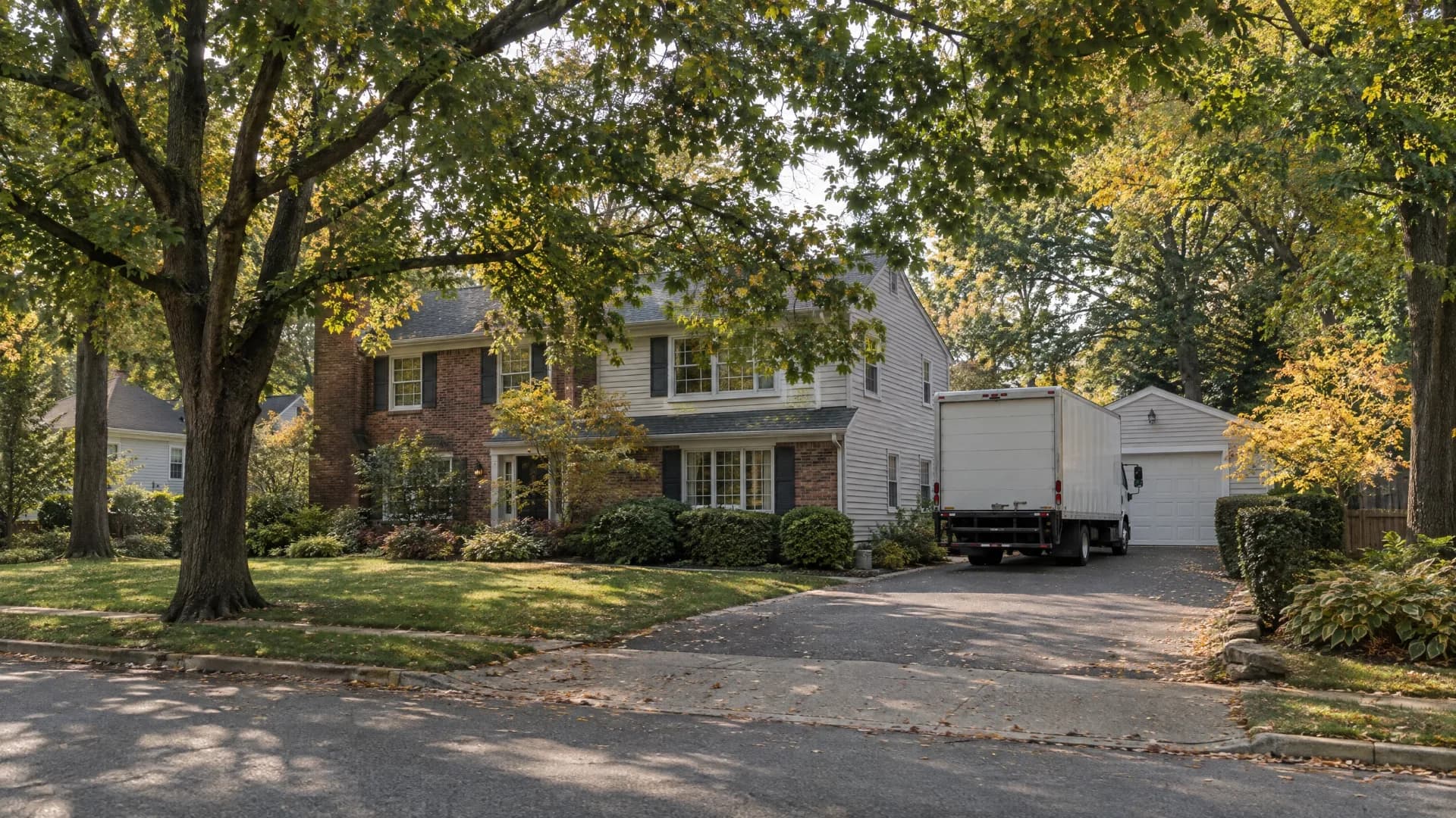 White moving truck on a tree-lined New Jersey suburban street beside a classic detached home