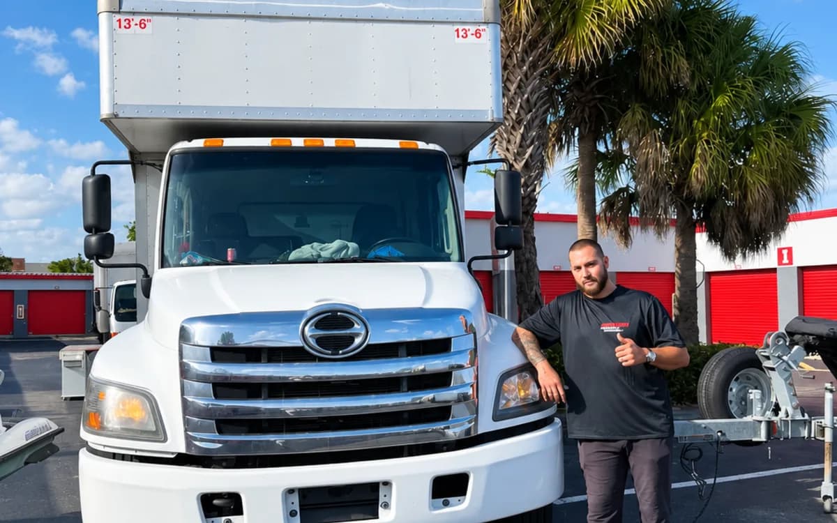 A branded Forward Moving & Storage truck parked beneath palm trees with a mover beside it