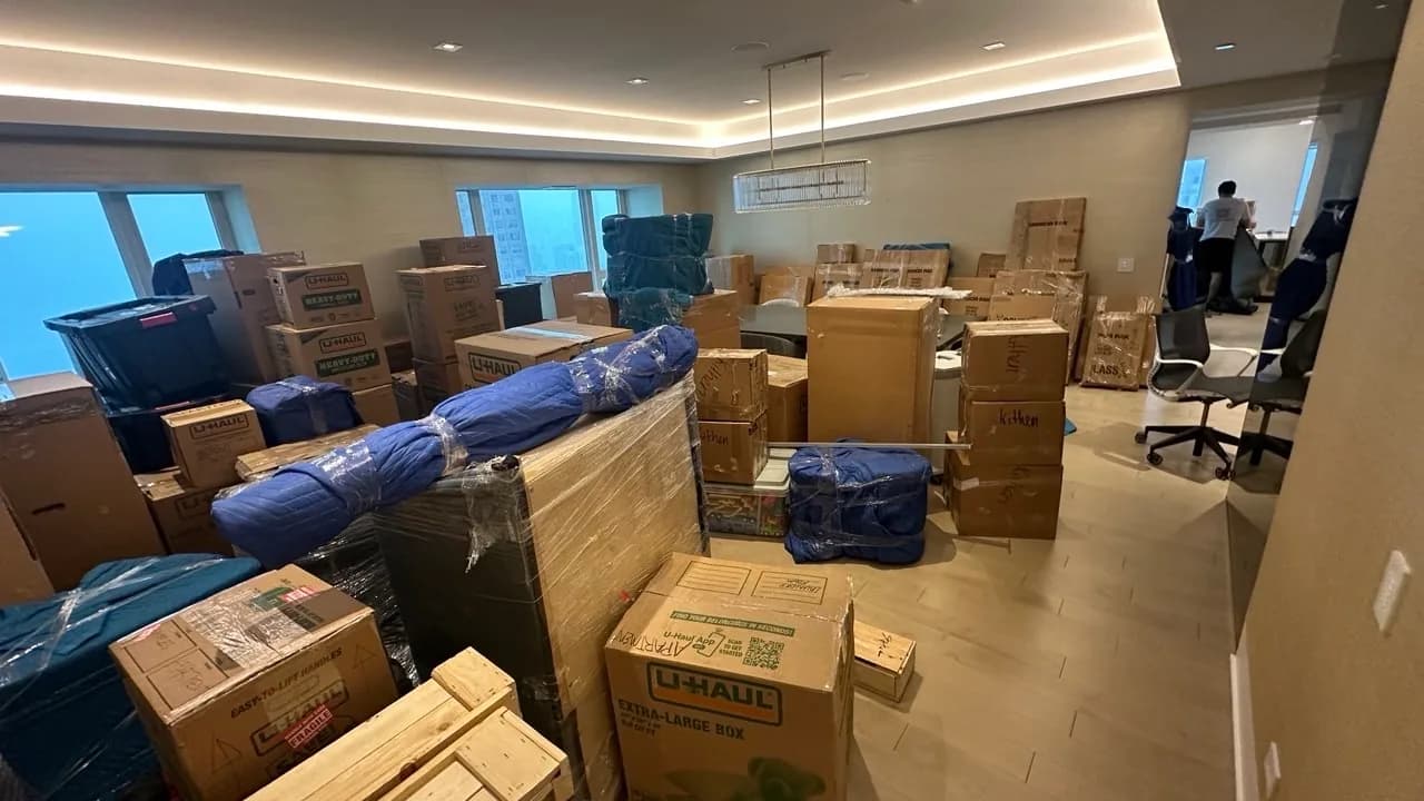 A living room packed for a move, with labelled boxes stacked and furniture wrapped in moving pads and plastic